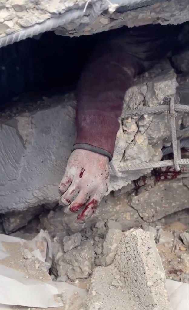 A child’s hand sticks out from underneath rubble in Gaza. Photo taken from a video by Motaz Azaiza, December 11, 2023.